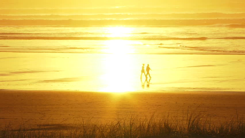 Man and woman walking during sunset at beach, dissolve into the sunlight