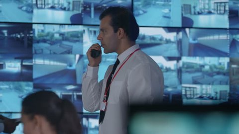 4K Security team watching CCTV screens in control room, officer talking on radio Dec 2016-UK