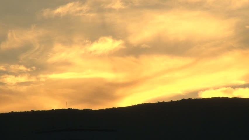 Sunset with orange lit clouds time lapse over hill. Reverse motion for great