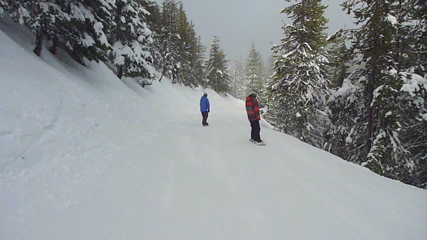Snowboarders and skiers travel down snowy hillside in winter.