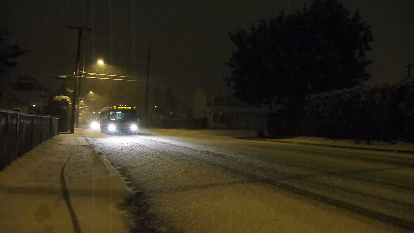 Fresh snow falls at night in Portland, Oregon as traffic including city busses