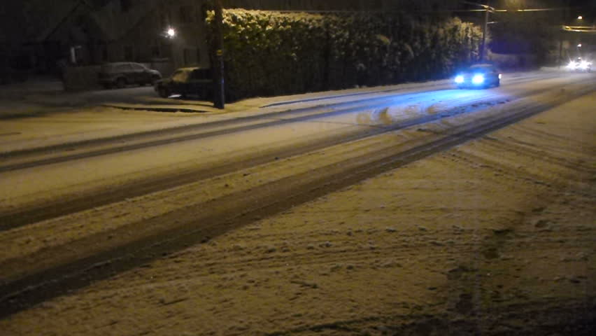 Fresh snow falls at night in Portland, Oregon as cars drive cautiously on roads.
