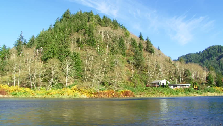 River front property with house sitting on water's edge in forest during autumn