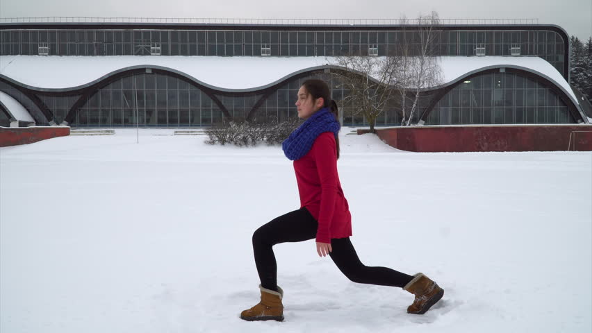 Young brunette woman performing a front lunge on a snowy field outdoors