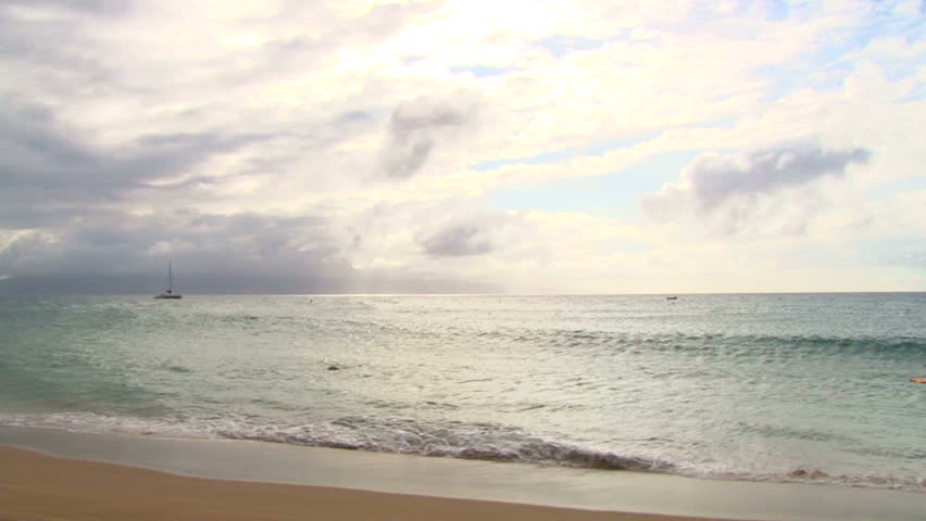 People playing and surfing the beach waves on the shores of Maui, Hawaii with sailboat in anchored.
