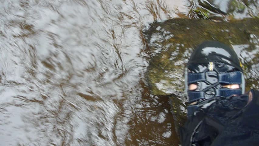 Man hikes through river in hiking shoes point of view.