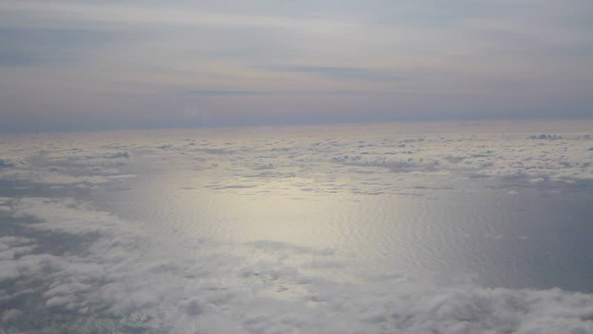 Flying in airplane passing clouds and sunny skies over the Pacific Ocean in