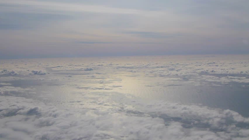 Flying in airplane passing clouds and sunny skies over the Pacific Ocean in