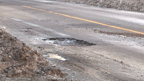 Pothole on city street causing damage to car tires if traffic passes over it.
