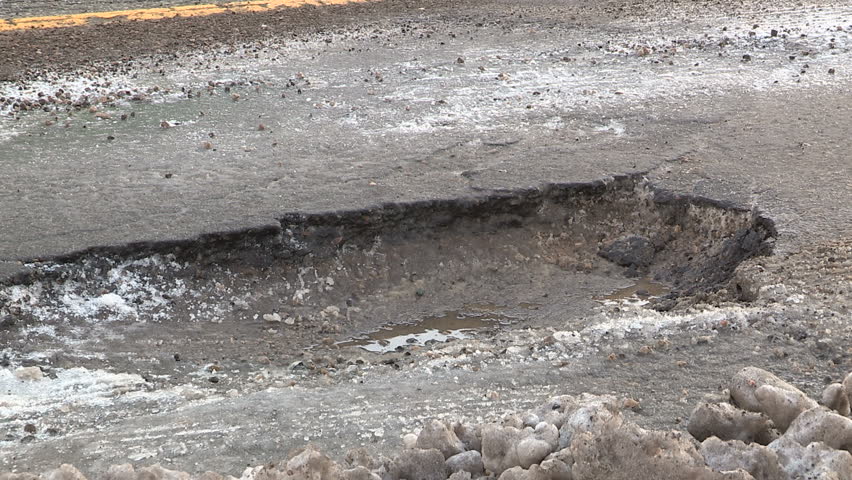 Pothole on city street causing damage to car tires if traffic passes over it.
