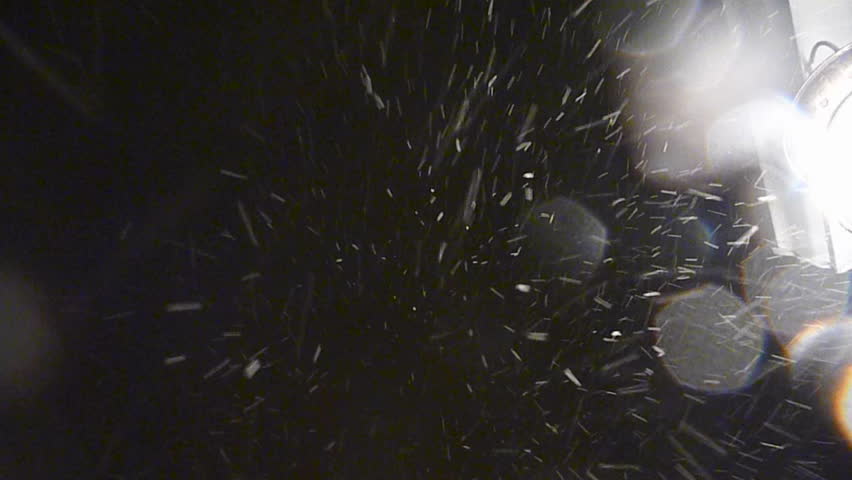 Fresh snow falls at night and hits camera lens.