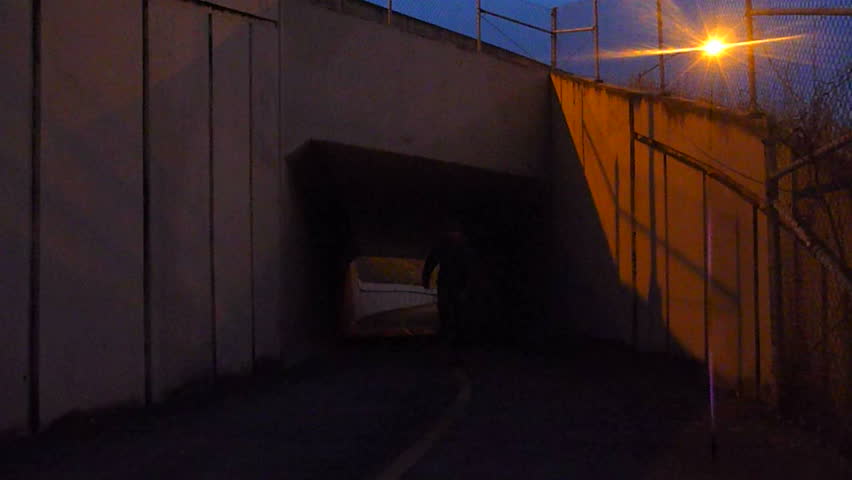 Man skateboards towards, up concrete pathway through tunnel with sound.