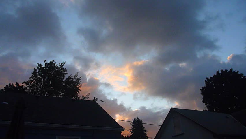 Clouds move fast over houses as sun sets in the evening time lapse.