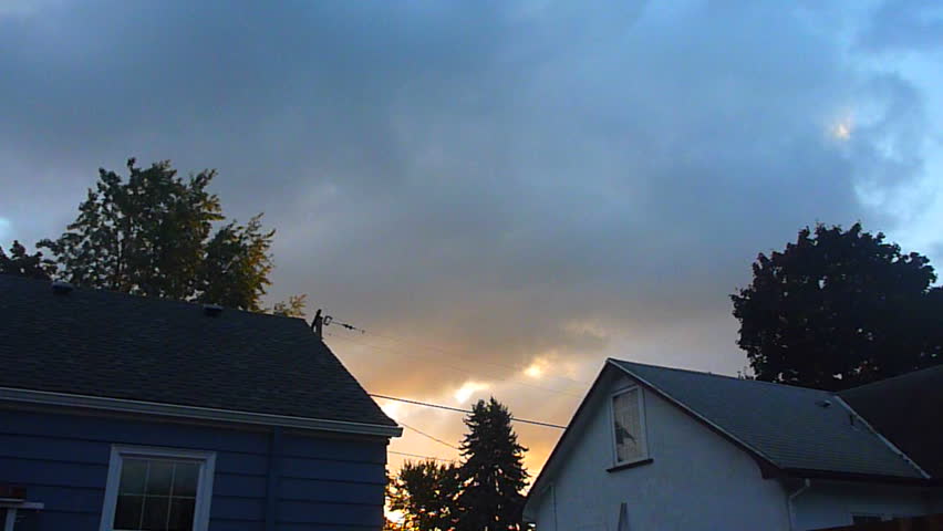 Clouds move fast over houses as sun rises in the morning time lapse.