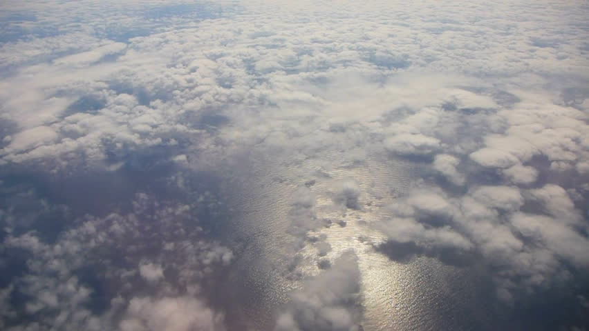 Flying in airplane over Pacific ocean and clouds with sun reflecting off water.