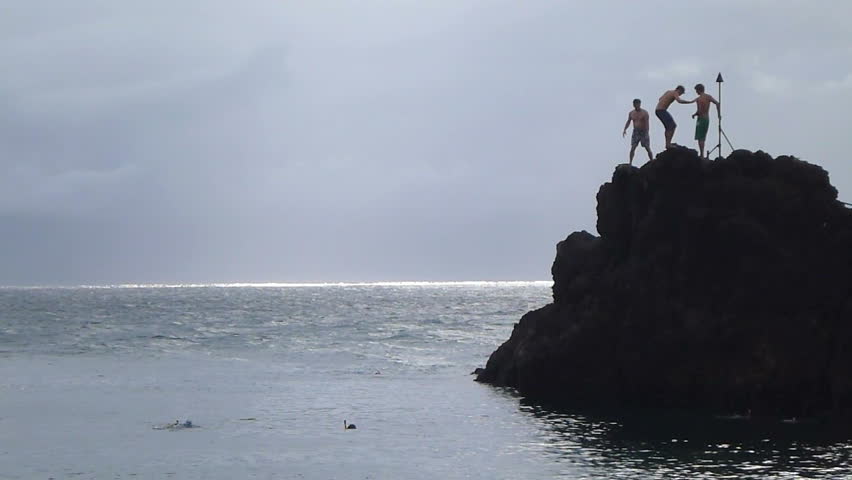 Person jumping off cliff by Black Rock at Kaanapali Beach in Maui, Hawaii near
