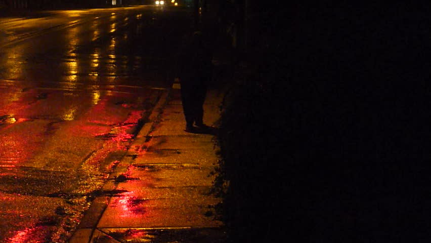 Mysterious person walks wet streets at night in rain storm.