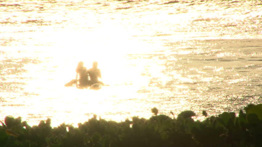Man and woman enjoying sunset on longboard in ocean off the shores of Maui,