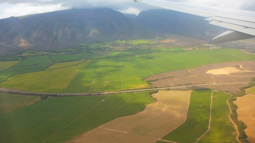 Flying in airplane over Maui Hawaii showing mountains and farm land.