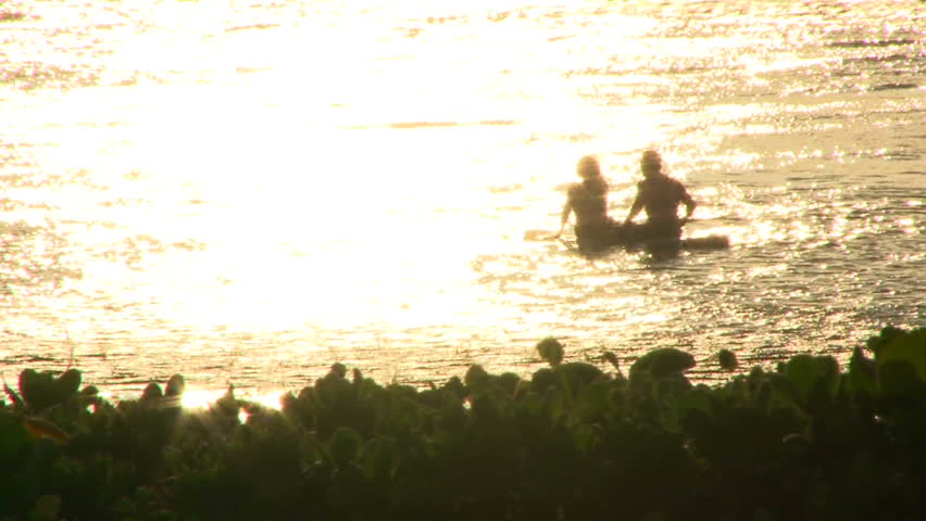 Man and woman enjoying sunset on longboard in ocean off the shores of Maui,