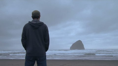 Time lapse of night clouds and man standing, watching Pacific Ocean.