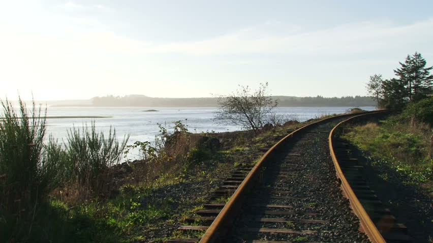 Man balances and walks along railroad tracks near waterway in Oregon.