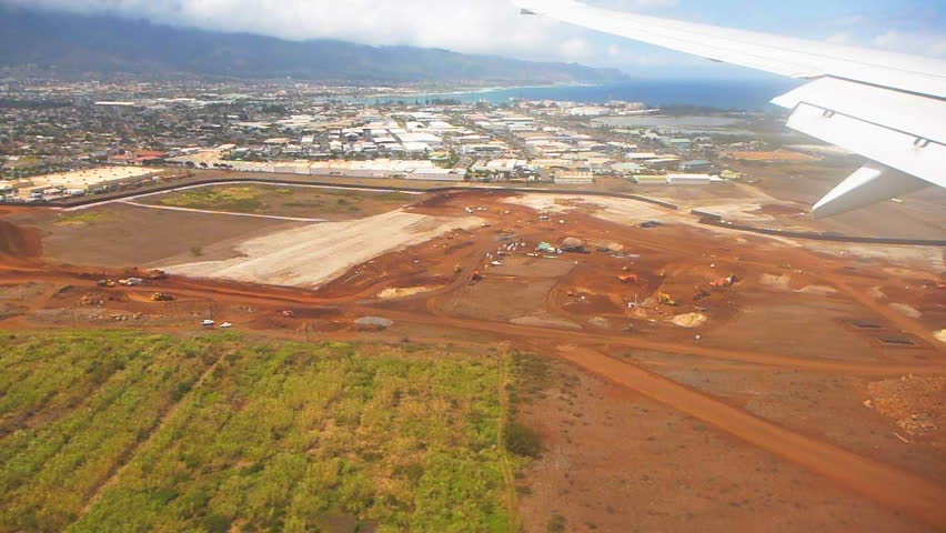 Flying in airplane and approaching airport over Maui Hawaii farm land and city