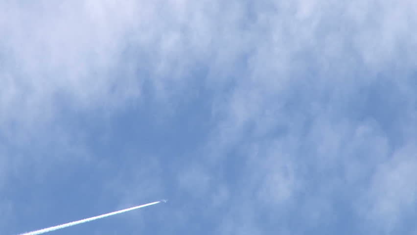 Airplane flies overhead on mostly sunny day leaving jet contrails behind.