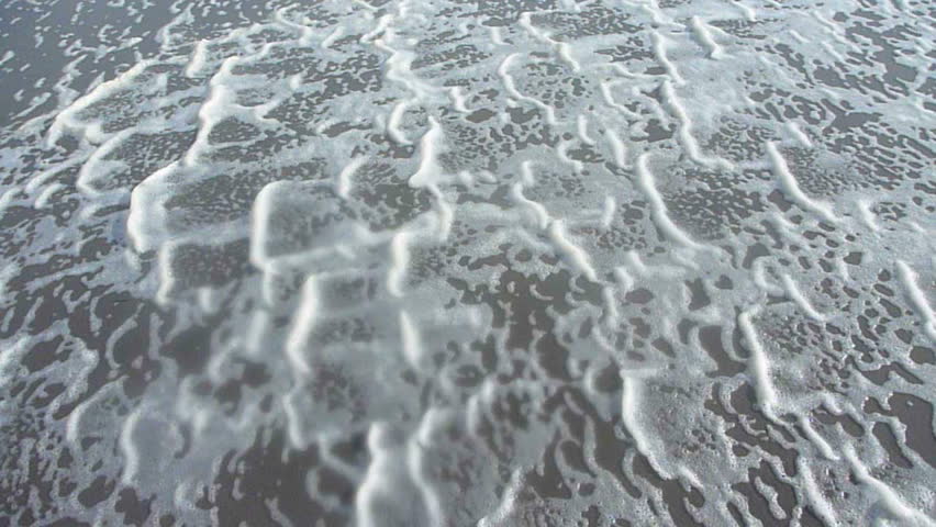 High winds blow ocean tide waters along sand.