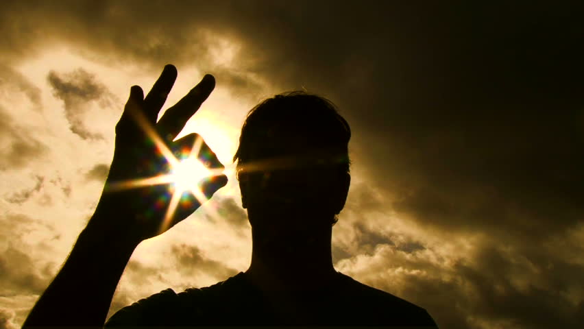 Person silhouetted raises hand into frame to give an a-okay sign with sun