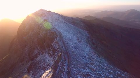 Aerial shot following the Snowdonia mountain railway to the summit of Snowdon at sunrise.