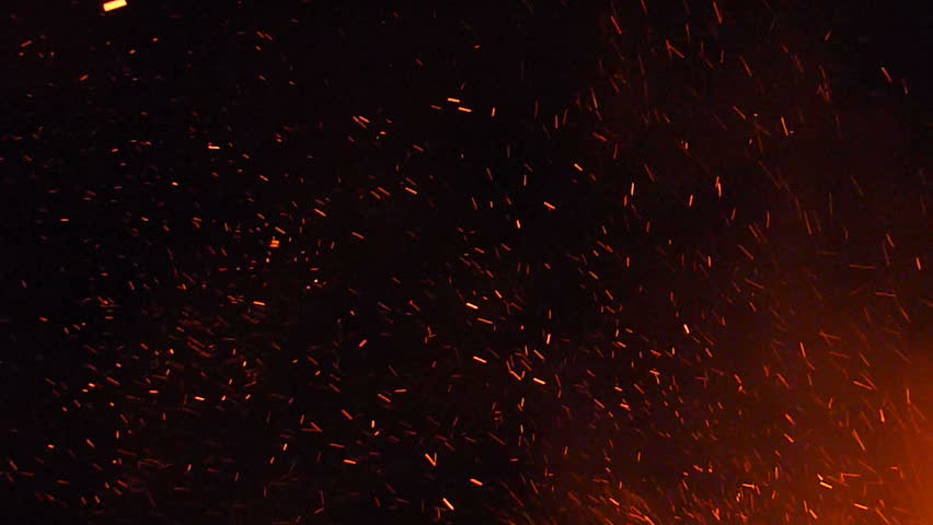 Burning ash rise from large fire in the night sky.