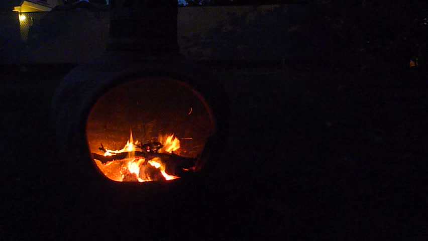 Time lapse of person feeding fire in chiminea at night.