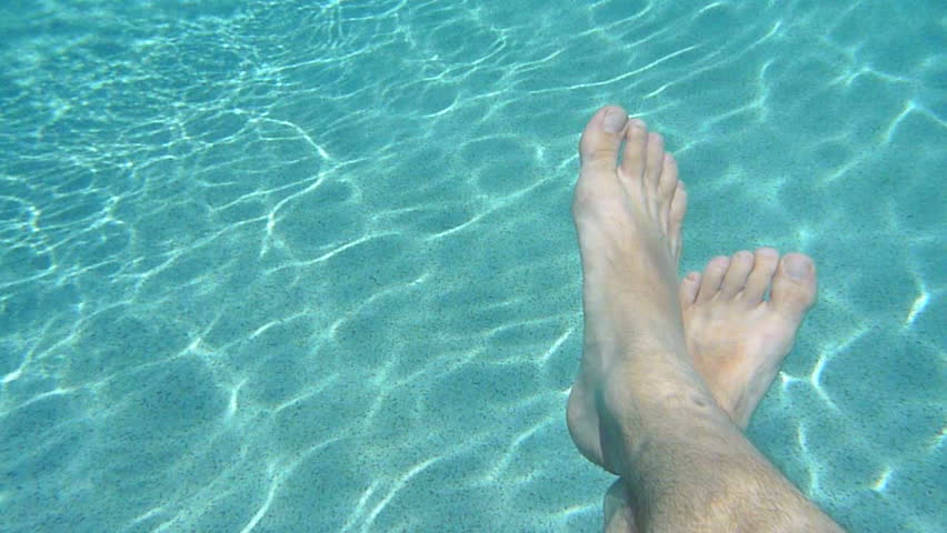 Man's feet relaxing and floating in swimming pool.