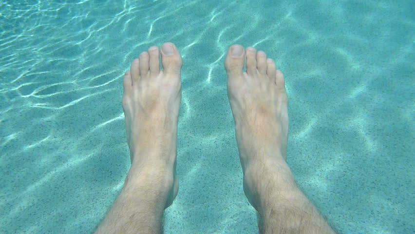 Man's feet relaxing and floating in outdoor swimming pool.