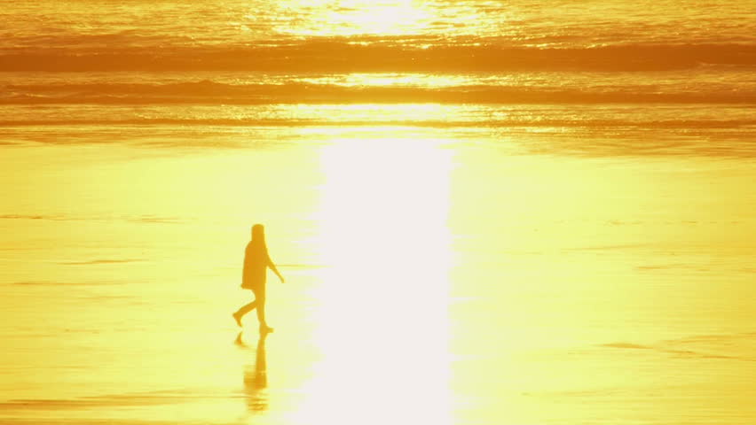 Woman walking during sunset at beach, dissolves into the sunlight reflection and