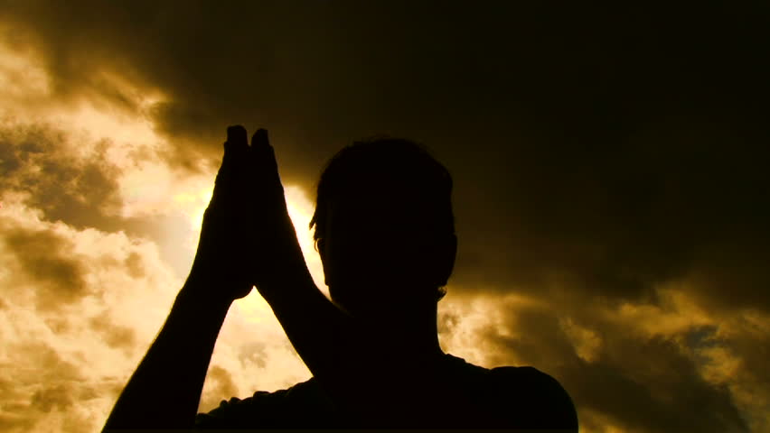 Person silhouetted separates praying hands to reveal sun shining through.