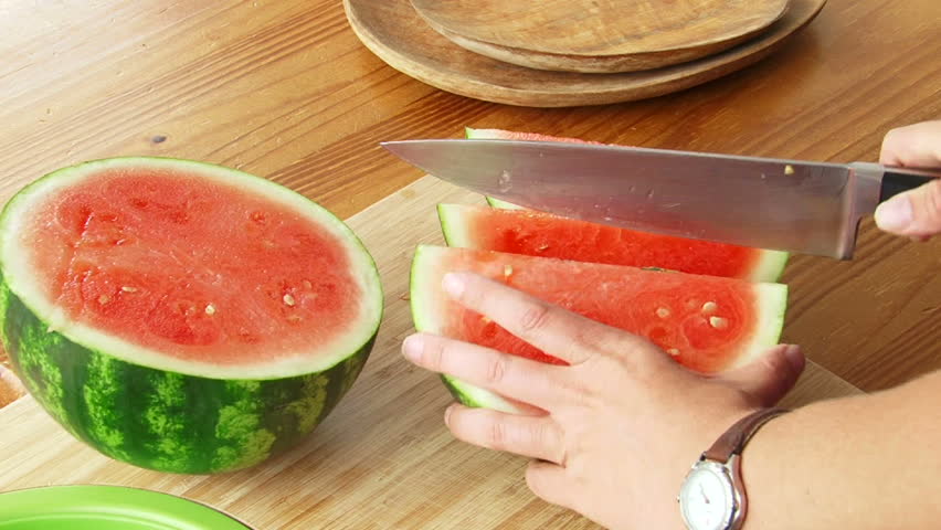 Woman cuts watermelon in slices with knife.