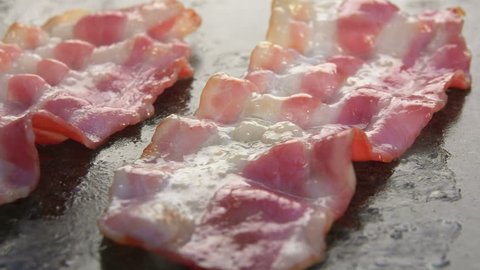 Bacon strips are fried and grilled on stone surface