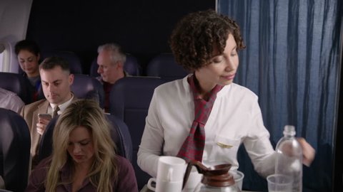 Flight attendant serving drinks and snacks to airliner passengers