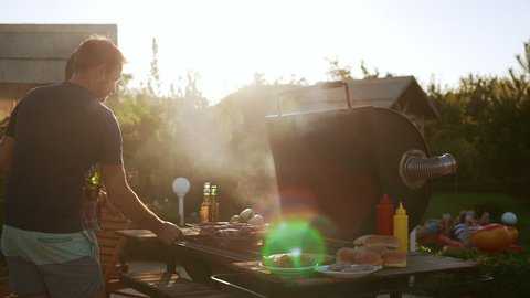 Two experienced males making barbecue with sausages outoddrs drinking beer in slowmotion