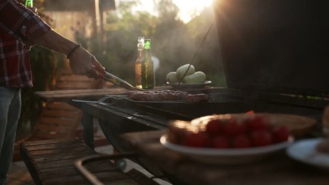Close up view of two men making barbecue outdoors drinking beer talking smiling in slowmotion. Close up