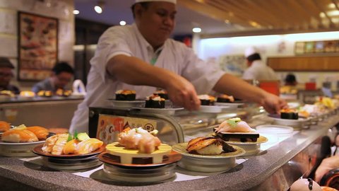 TOKYO, JAPAN - OCTOBER 10, 2014: A chef prepares sushi as other dishes go around on the conveyor belt in a busy open kitchen Japanese restaurant on October 10, 2014 in Tokyo, Japan