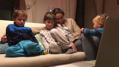Children and mom watching TV screen on sofa. Candid natural authentic shot of mom watching TV with her children on sofa