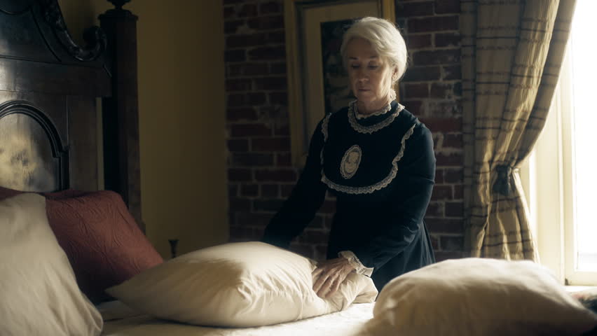 Mature Victorian era woman with white hair making the bed in her home 4k