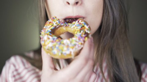 Close up of a woman who is eating donut with colorful frosting and smiling.
