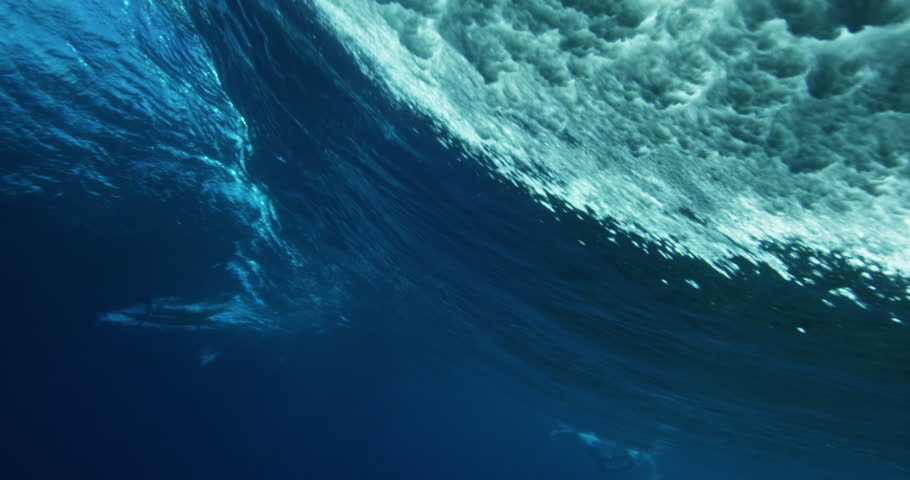 Under water view of blue ocean wave from behind. Barreling wave with sunlight and bubbles
