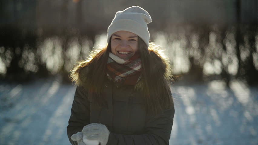 Cheery Active Woman is Throwing Snowball at the Camera Having Fun Outdoors during Winter Time. Smiling Girl Enjoying Cold Sunny Morning in the Park.