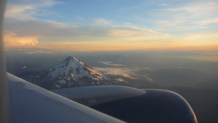 Flying in airplane through clouds over Portland, Oregon and Mt Hood at sunset.
