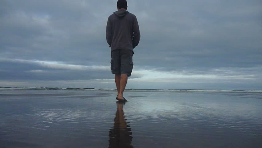Man walks sandy beach towards Pacific Ocean in Oregon.